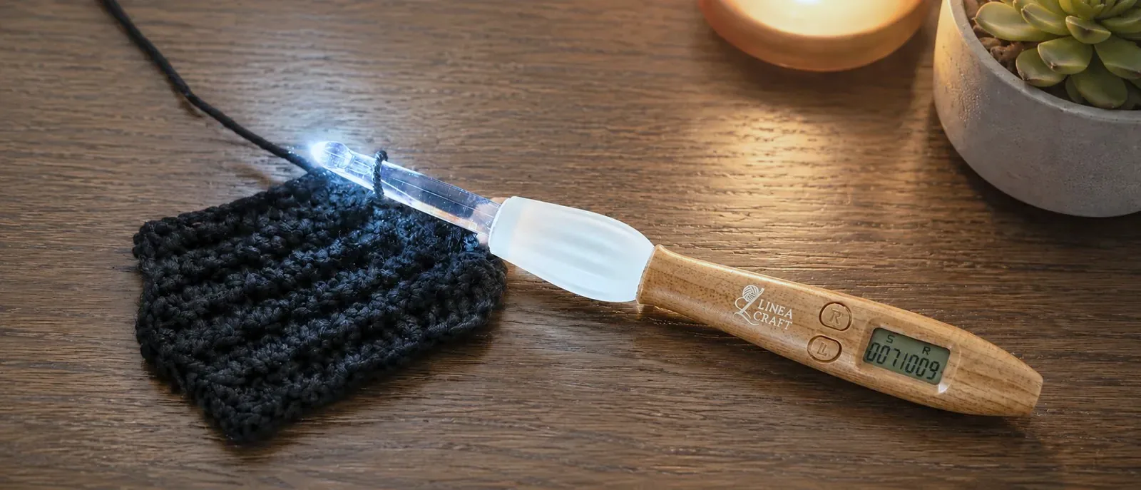 Counting crochet hook with its tip glowing, resting on black crochet on a wooden table