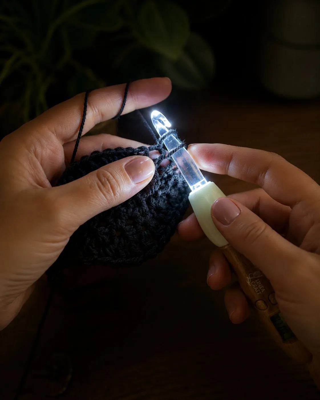 Hands crocheting black yarn in a dark room, the hook tip glowing white