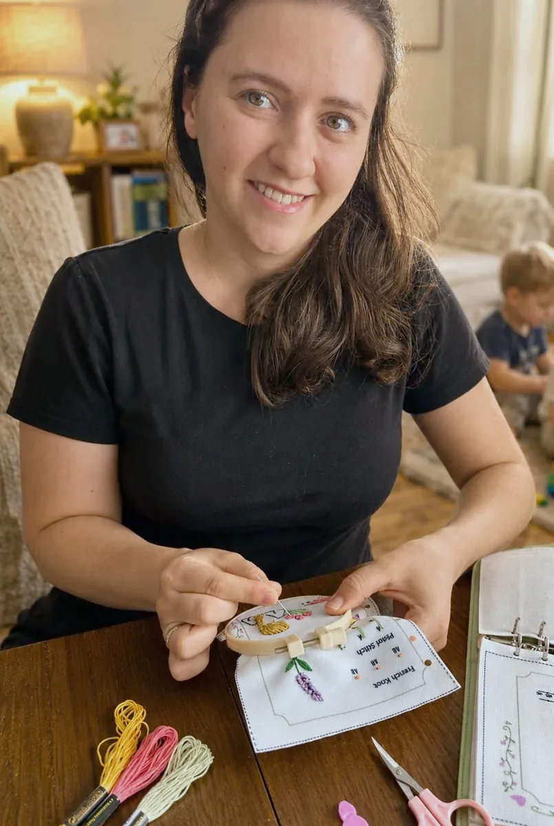 Diana embroidering a page from the Stitch Book at home while her son plays nearby