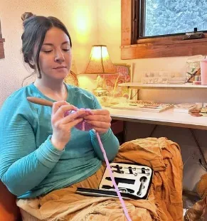 Crocheter working on a pink project at her desk with the case beside her